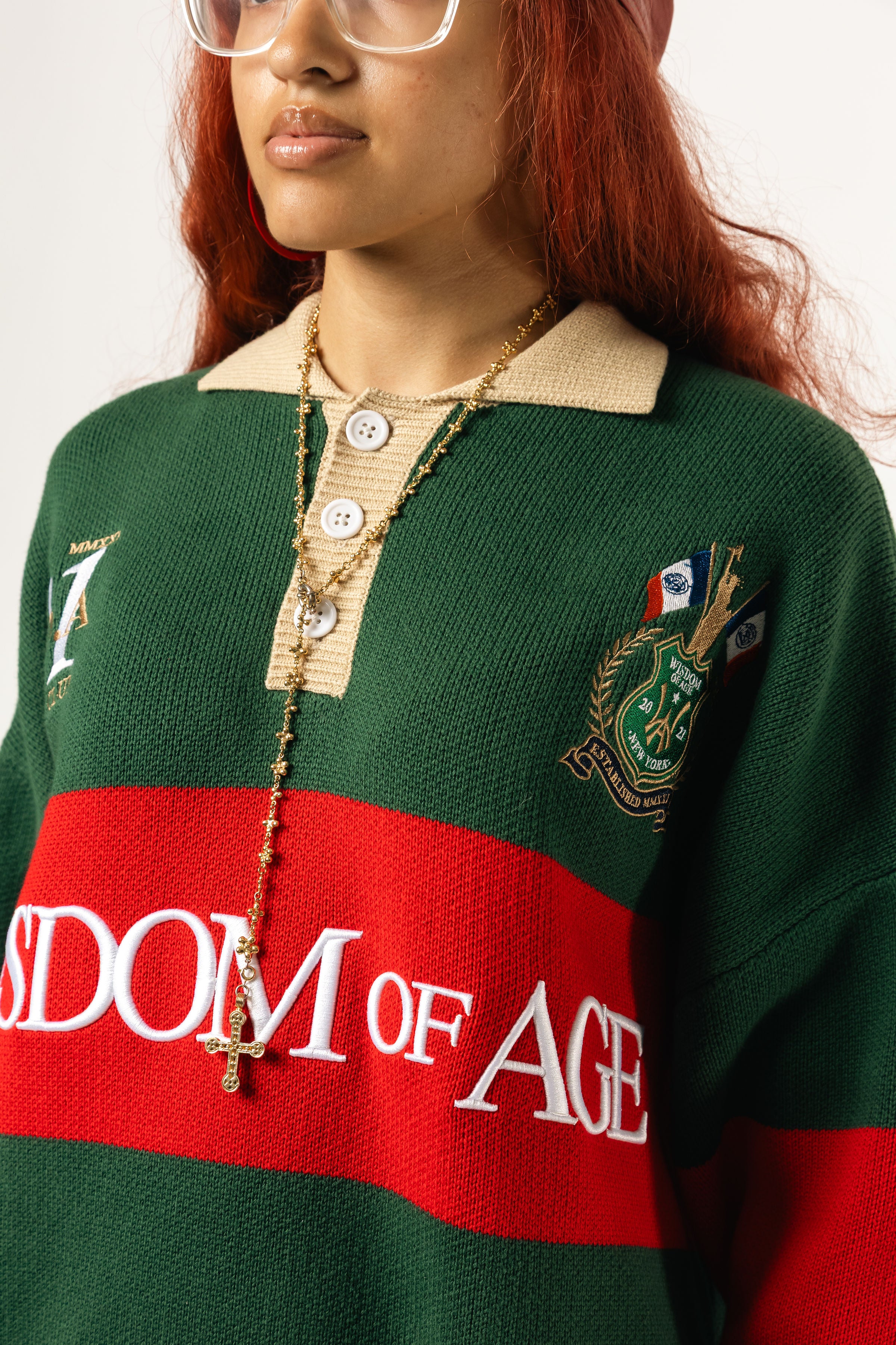 Close up of a female Model wearing a green and red, knitted rugby sweater with 'Wisdom of Age' text on a white background.
