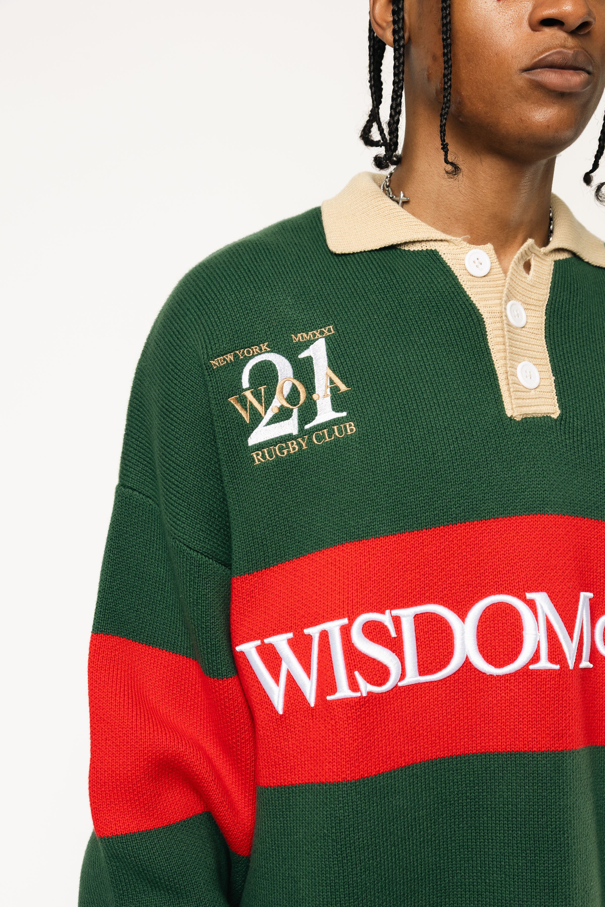 Close up of Male Model wearing a green and red, knitted rugby sweater with 'Wisdom of Age' text on a white background.