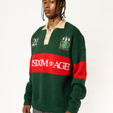 Front-side view of a Male Model wearing a green and red, knitted rugby sweater with 'Wisdom of Age' text on a white background.
