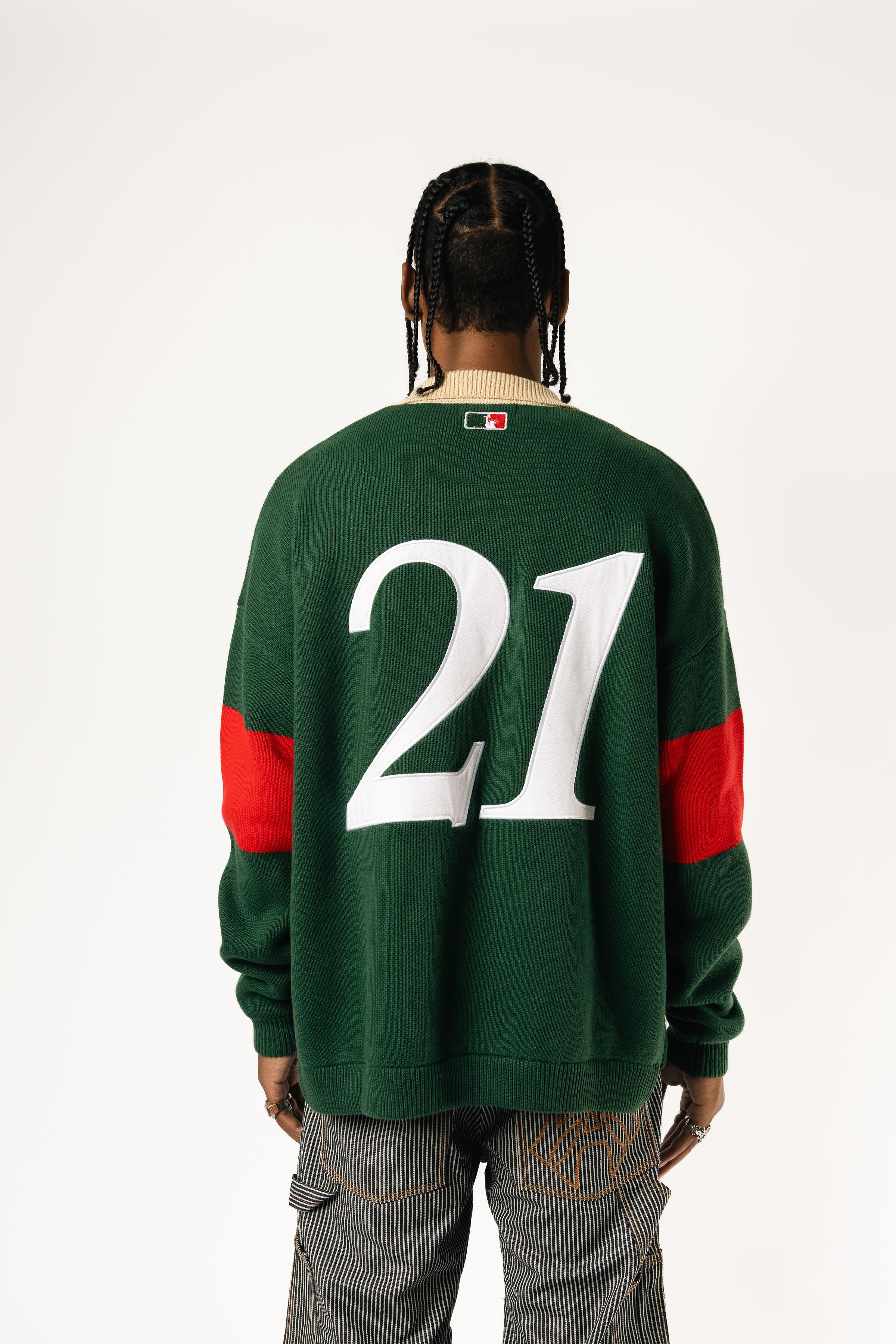 Rear view of a Male Model wearing a green and red, knitted rugby sweater with '21'  on a white background