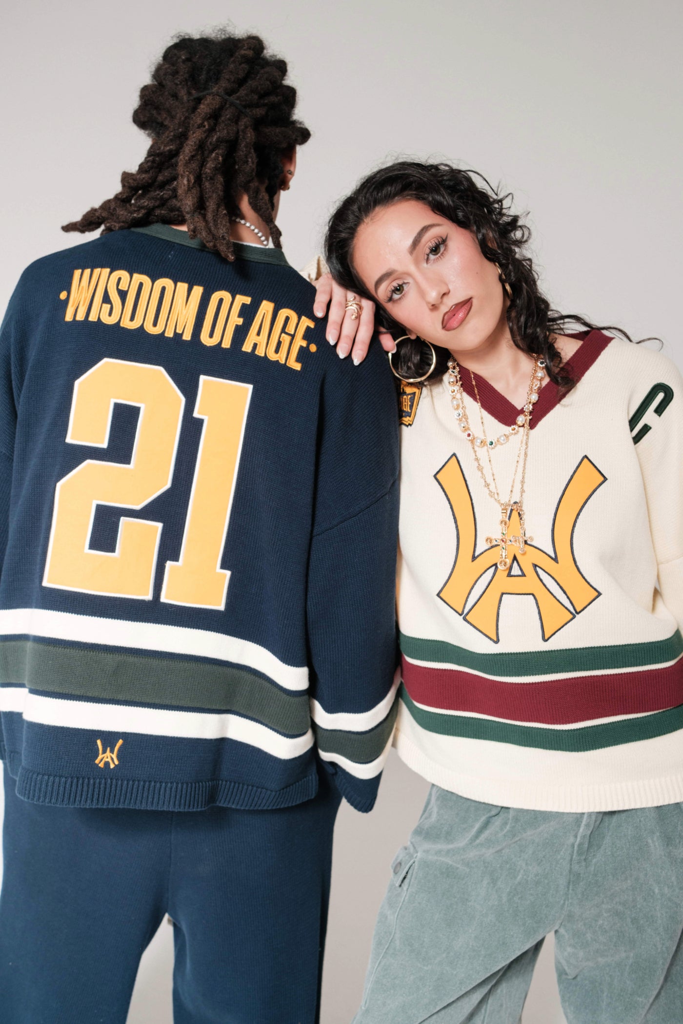 Male showing the back of the Wisdom Of Age Hockey Jersey in Navy. Wisdom Of Age written across the back in yellow with the number 21 underneath. Female mode wearing the WOA Hockey jersey Cream V2. Yellow WA logo on the front. 