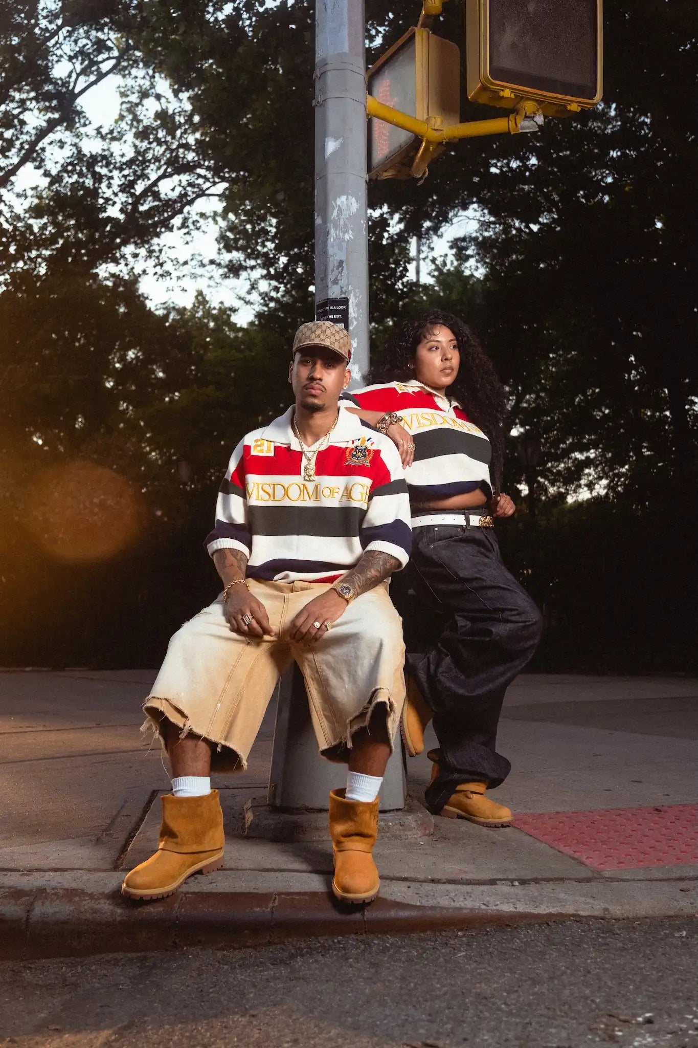 Male and female models wearing Wisdom Of Age Multicolor Rugby Polos while leaning on lamppost 