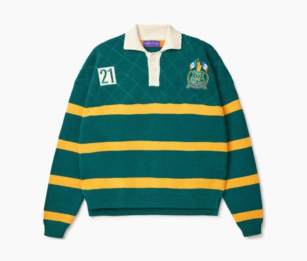 Front View of the Wisdom of age Lemon rugby. This is a Green garment with yellow stripes, a cream collar and buttons. There is a Wisdom of age NY state patch on the left shoulder and a embroidered number 21 within a cream box 