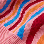 Close-up of a knitted fabric with colorful wavy pattern on pink background