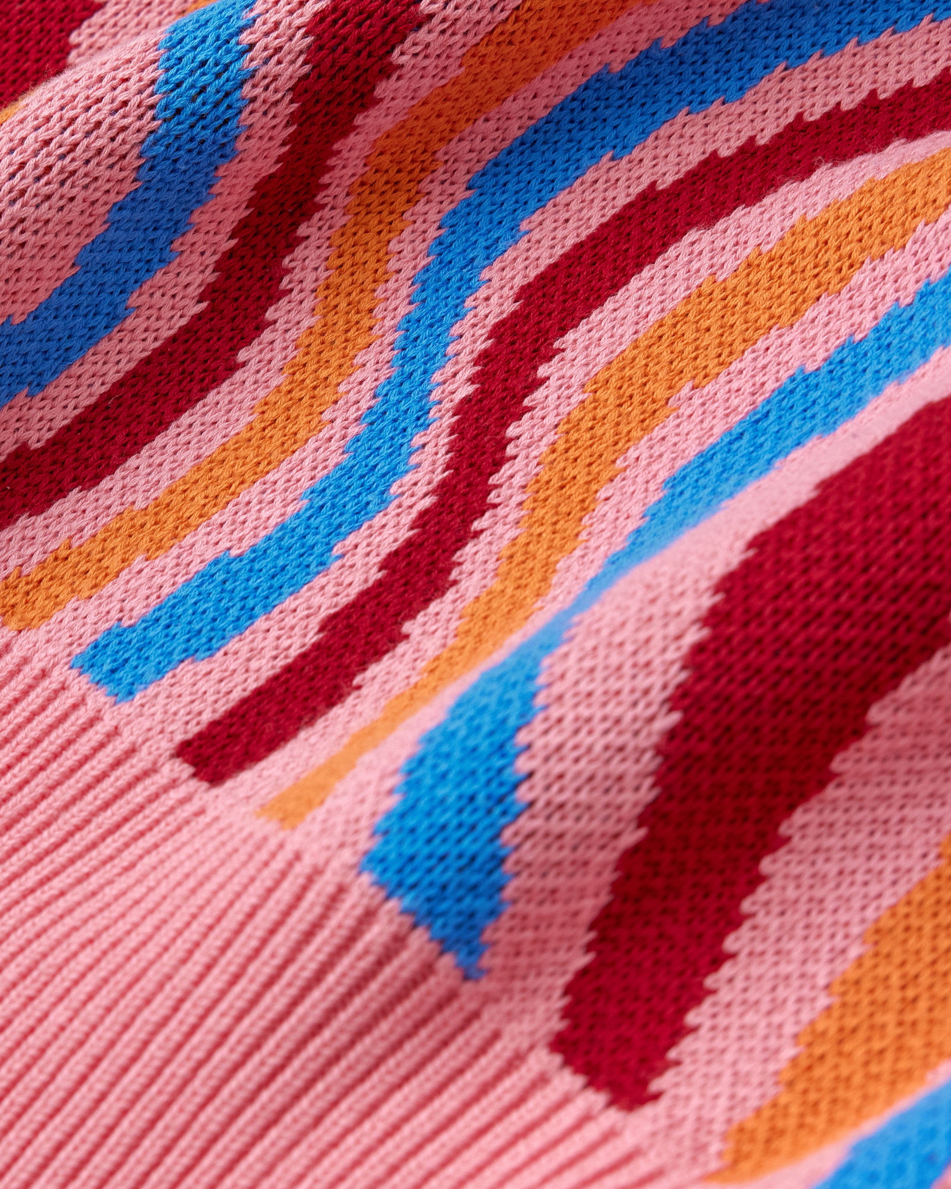 Close-up of a knitted fabric with colorful wavy pattern on pink background