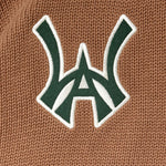 Close-up of a green WA logo with white outline on a brown textured background
