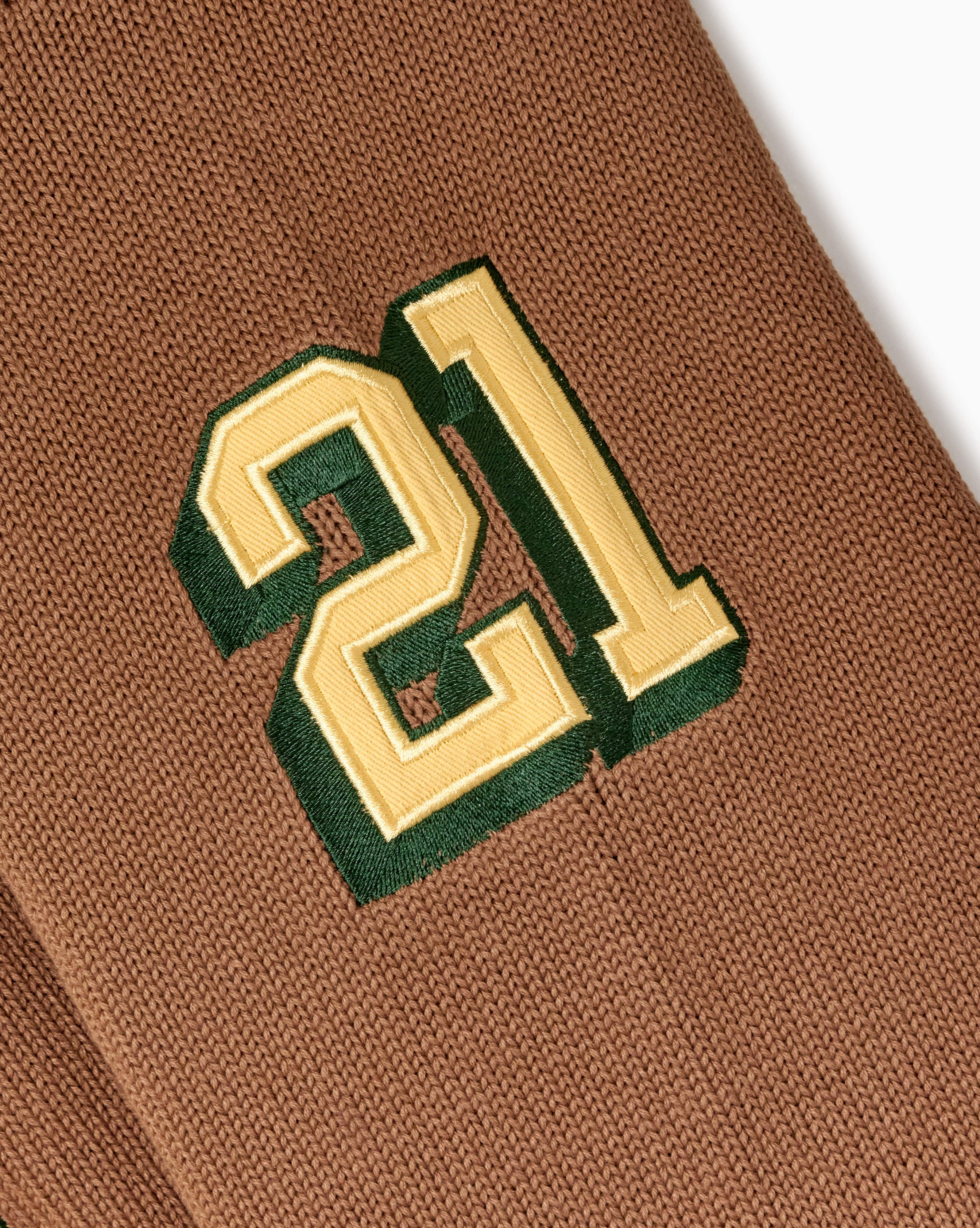 Close-up of a brown fabric with a green and gold number '21' embroidered on it.