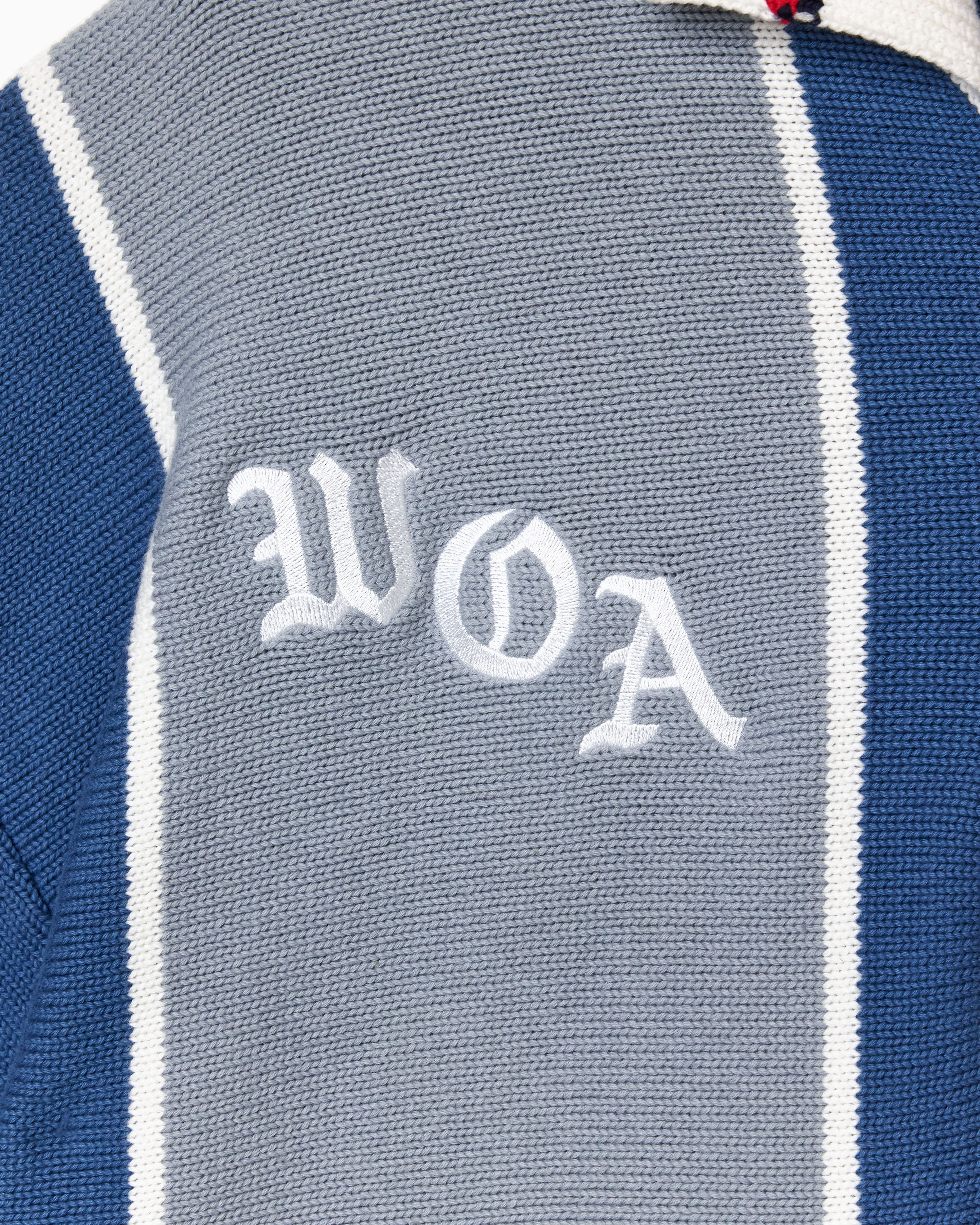 Close-up of a knitted soccer jersey with 'WOA' embroidery on a blue and gray background