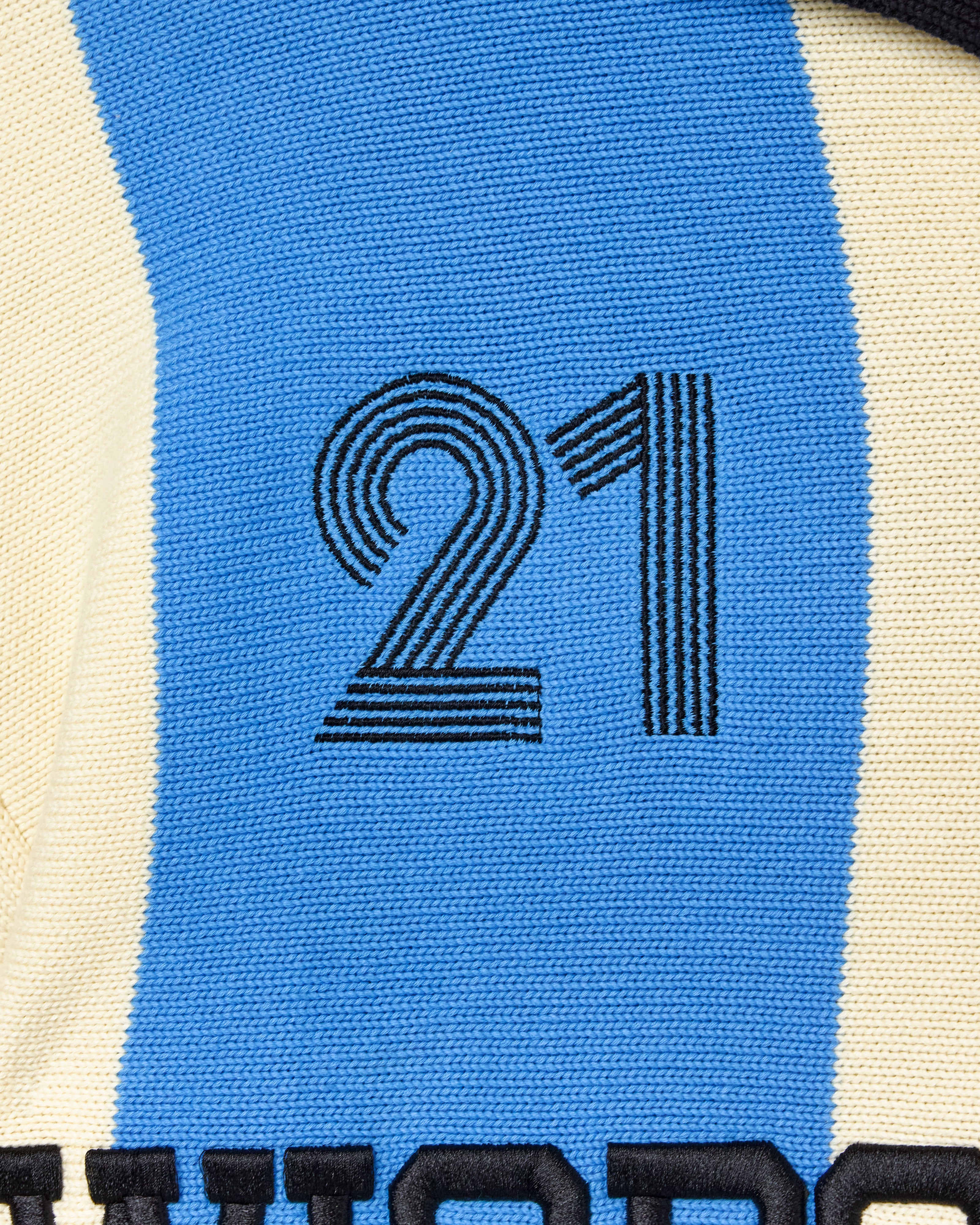 Close-up of the Wisdom Of Age Knit Soccer Jersey Celeste. A knitted soccer jersey with number 21 on a blue and beige background