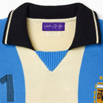 Close-up of a blue and beige knitted soccer jersey with the Wisdom Of Age label on a white background