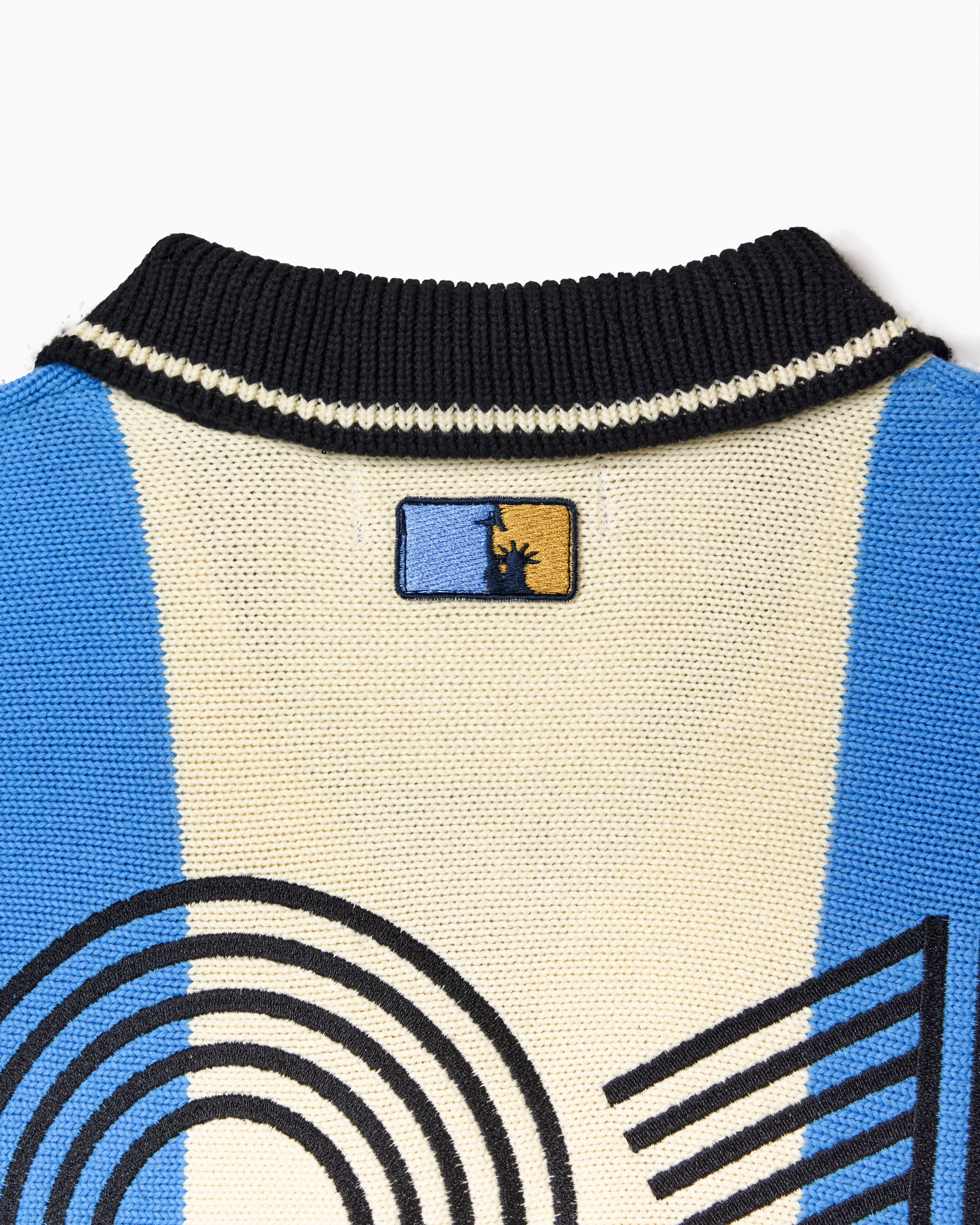 Close up Of the Wisdom Of Age Knit Soccer Jersey Celeste. Blue and beige striped Knitted Soccer Jersey with 'NY TOUGH' logo on a white background