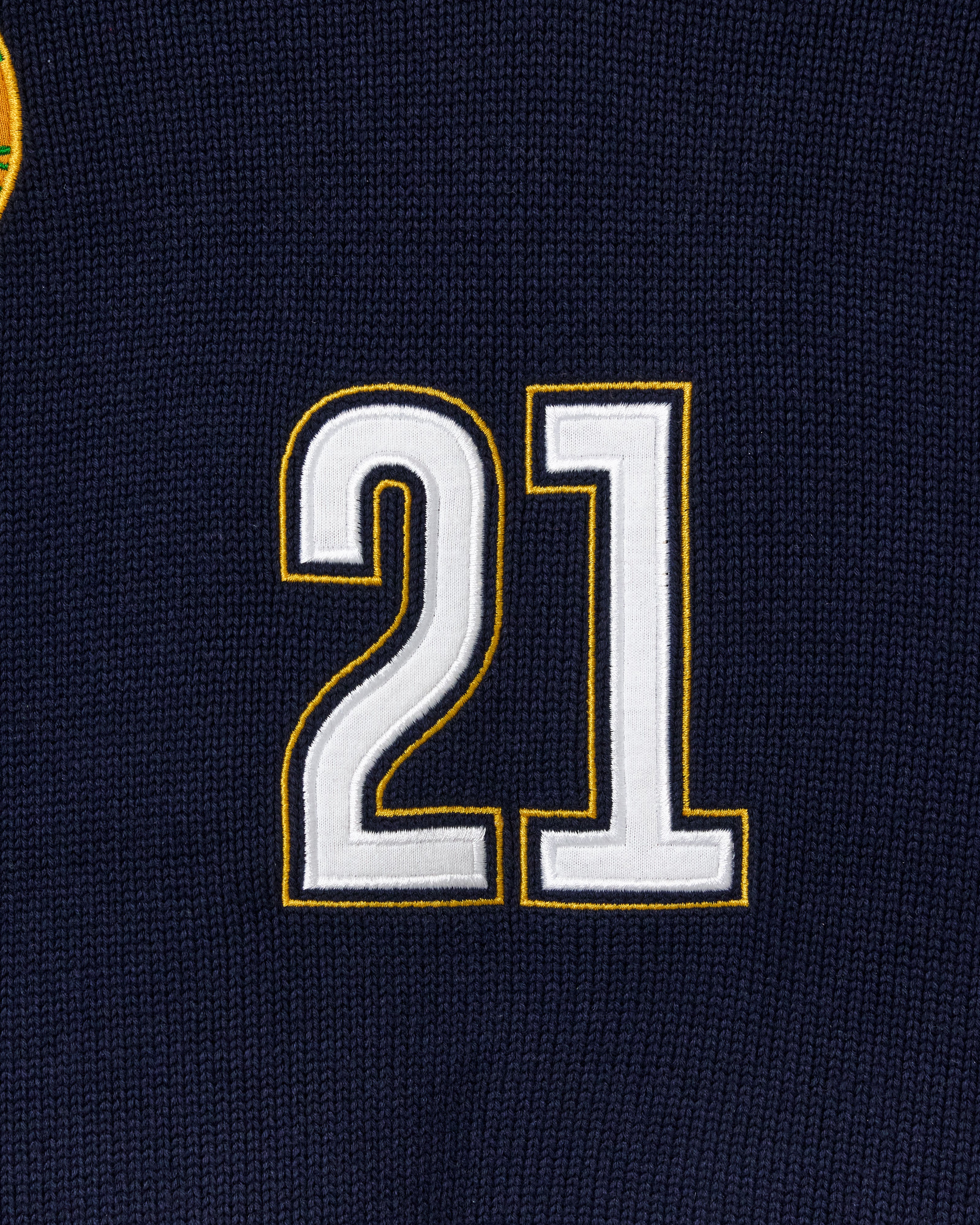 Wisdom Of Age Knit Soccer Jersey RIo. Close-up of a black knitted soccer jersey with the number 21 embroidered in white and gold.