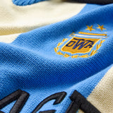 Close-up of The Wisdom Of Age Knit Soccer Jersey Celeste with a logo and text on a blue and beige background