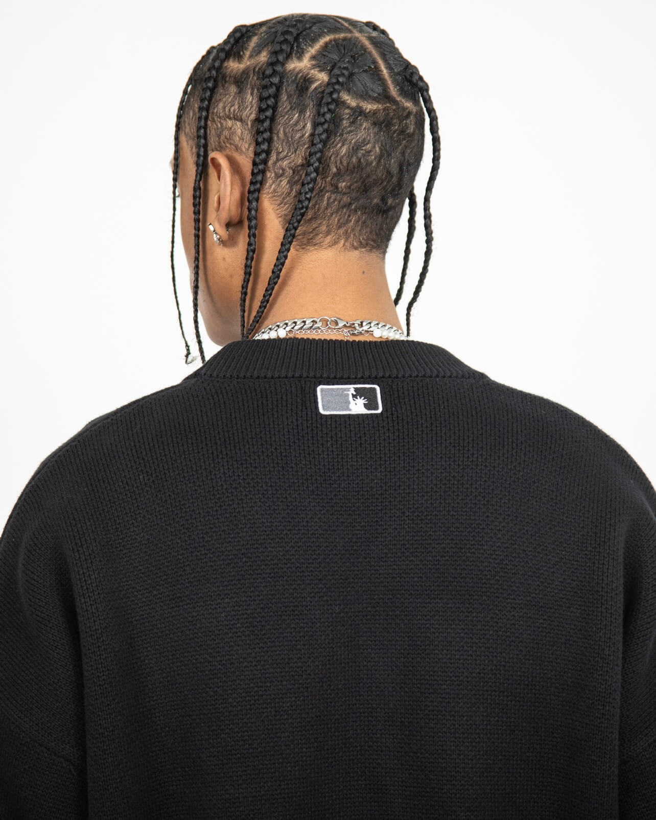 Closer look at the back of the sweater with an embroidered square patch below the nape of the neck and collar. The patch contains the upper half of the Statue of Liberty in a "NY Tough" inspired logo.