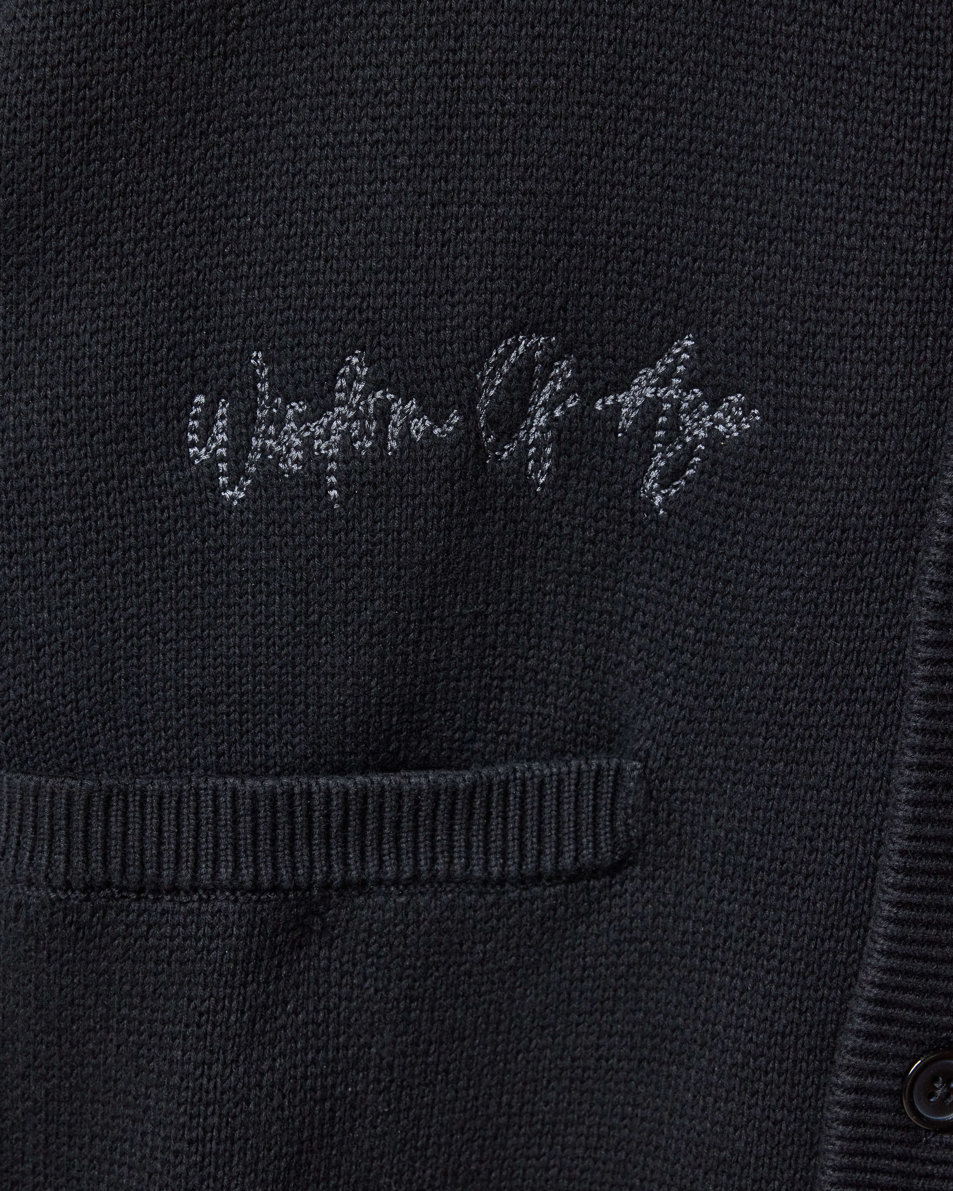 Closer Look at top right chest of the front of the cardigan with the brand name "Wisdom of Age" embroidered in a handwritten script cursive.