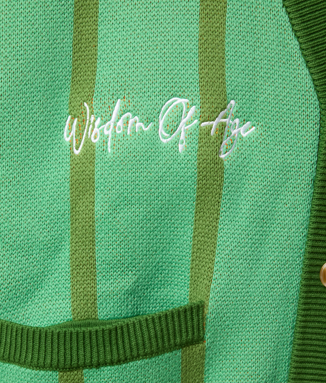 Closer Look at top right chest of the front of the cardigan with the brand name "Wisdom of Age" embroidered in a handwritten script cursive.