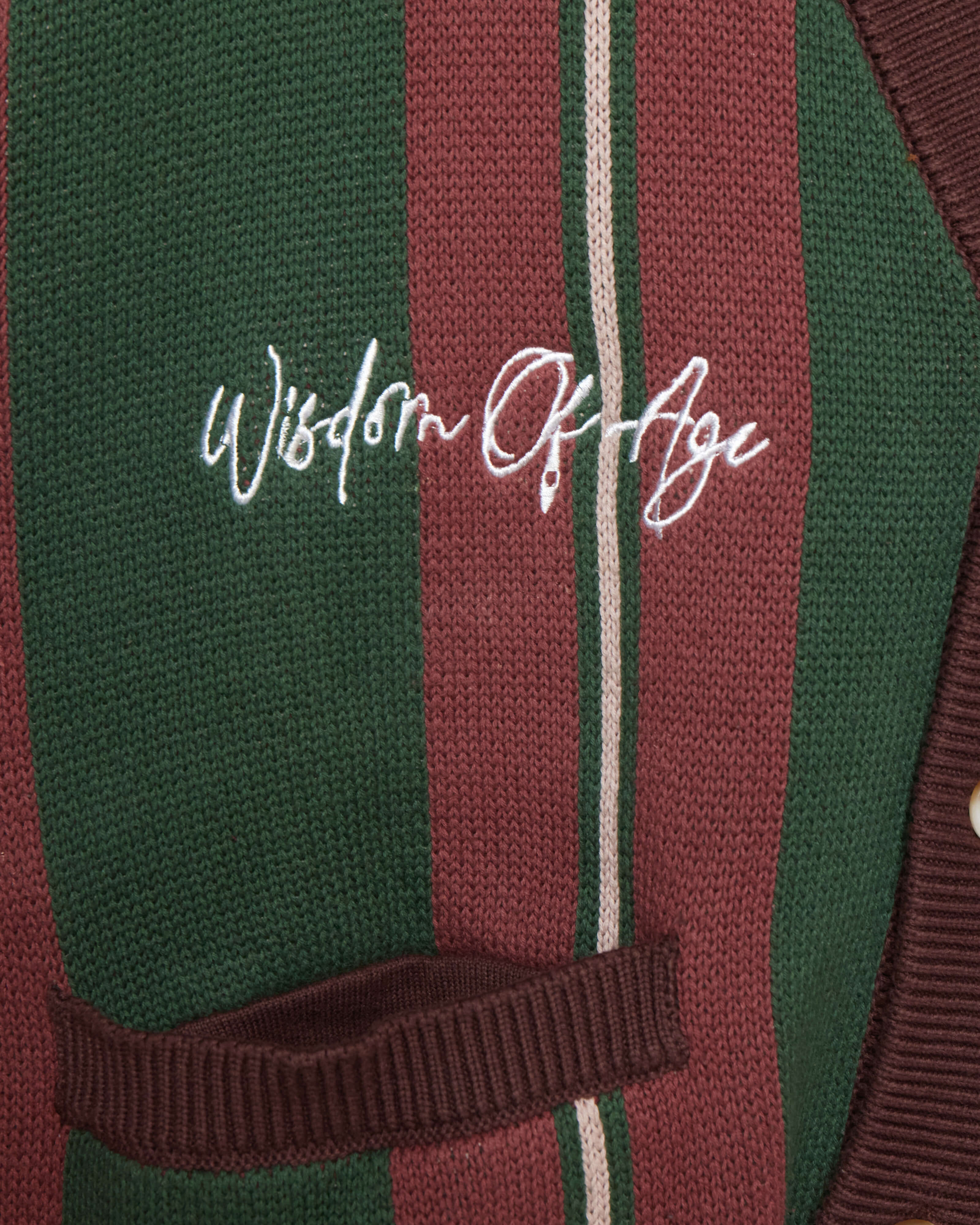 Closer Look at top right chest of the front of the cardigan with the brand name "Wisdom of Age" embroidered in a handwritten script cursive.