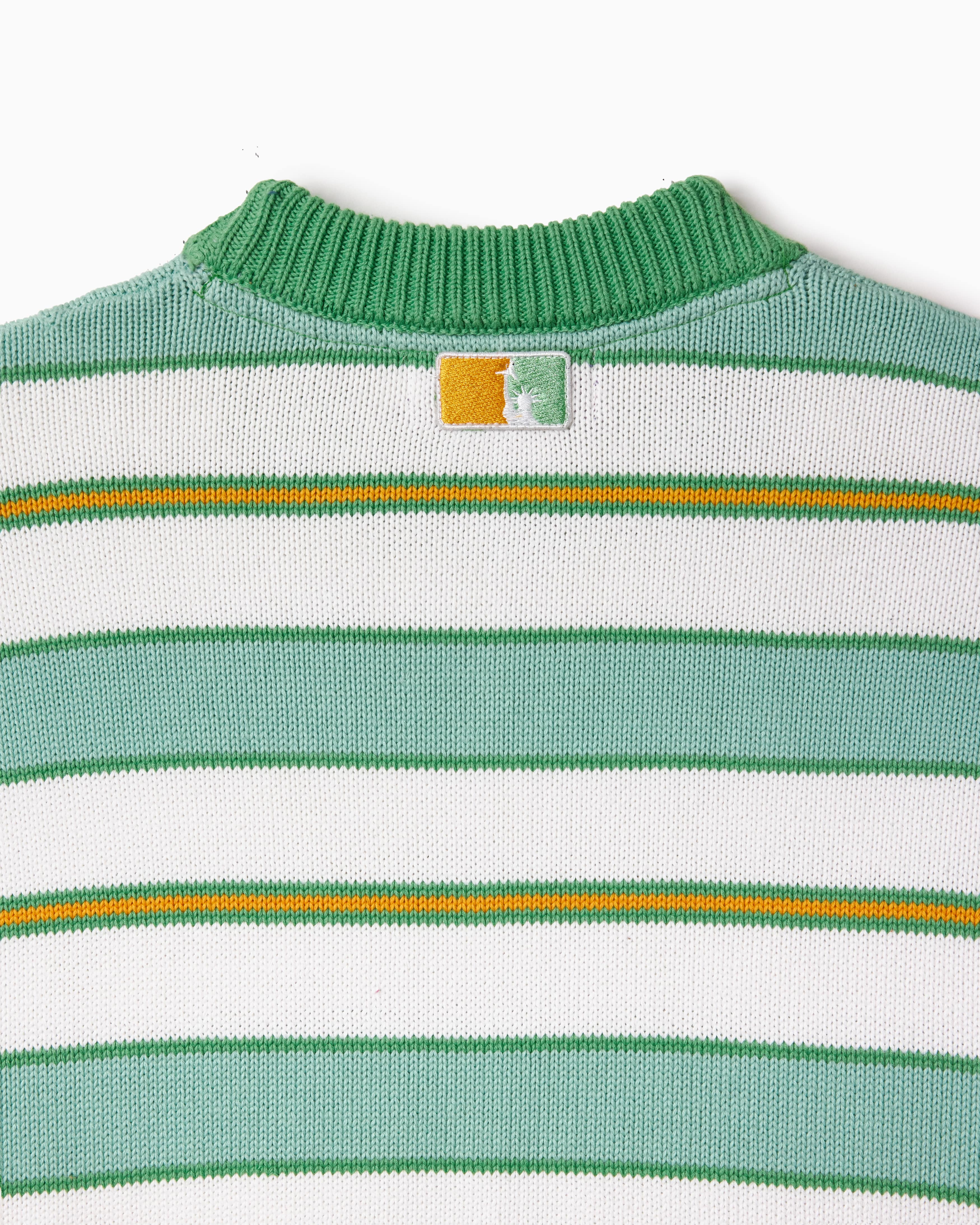Close-up of a green, yellow and white striped sweater with a the WOA Liberty logo on a white background