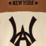 Close-up of the Wisdom Of Age Knit Football Jersey showing the WA logo with 'New York' on the nameplate  on a brown and beige background