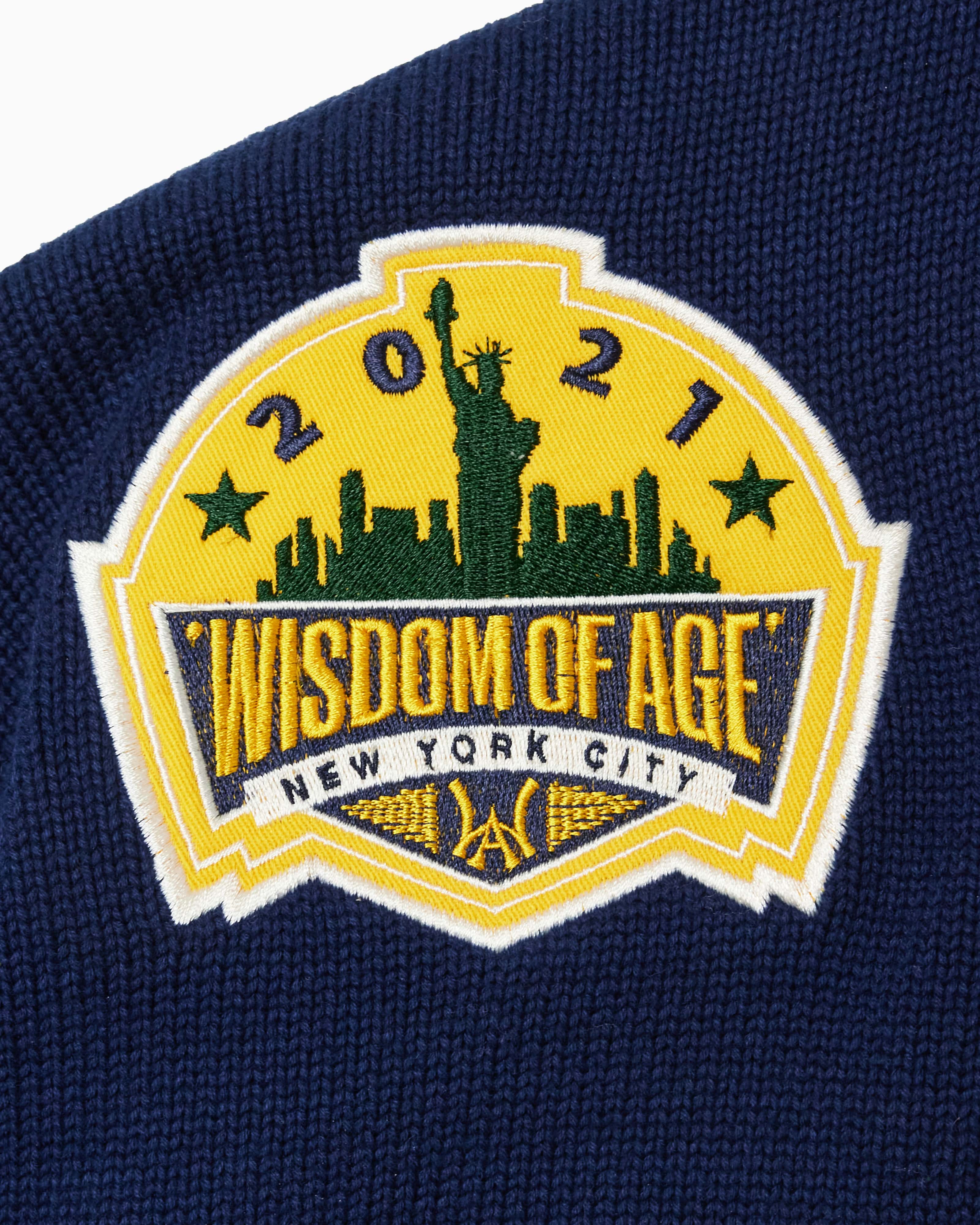 Close Up Of The Wisdom Of Age Knit Hockey Jersey Navy Front Patch.