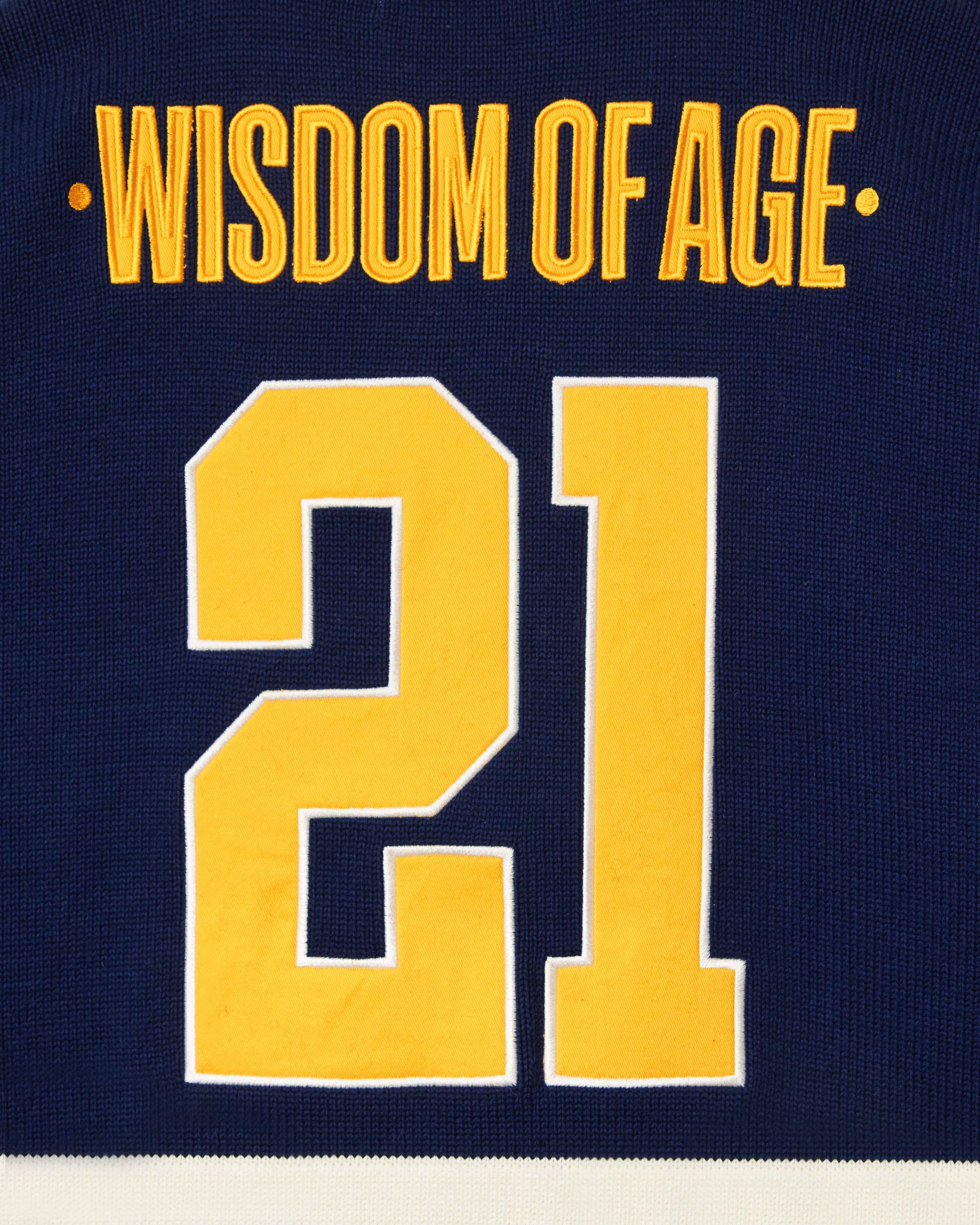 Close Up Of The Wisdom Of Age Knit Hockey Jersey Navy Rear View. Wisdom Of Age on the nameplate. The number 21 under.