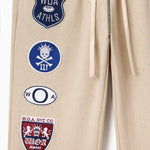 Wisdom Of Age Sandstone sweat pants with various patches including W.O.A and W.O.A.NYC.CO logos.