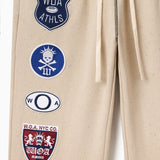 Wisdom Of Age Sandstone sweat pants with various patches including W.O.A and W.O.A.NYC.CO logos.