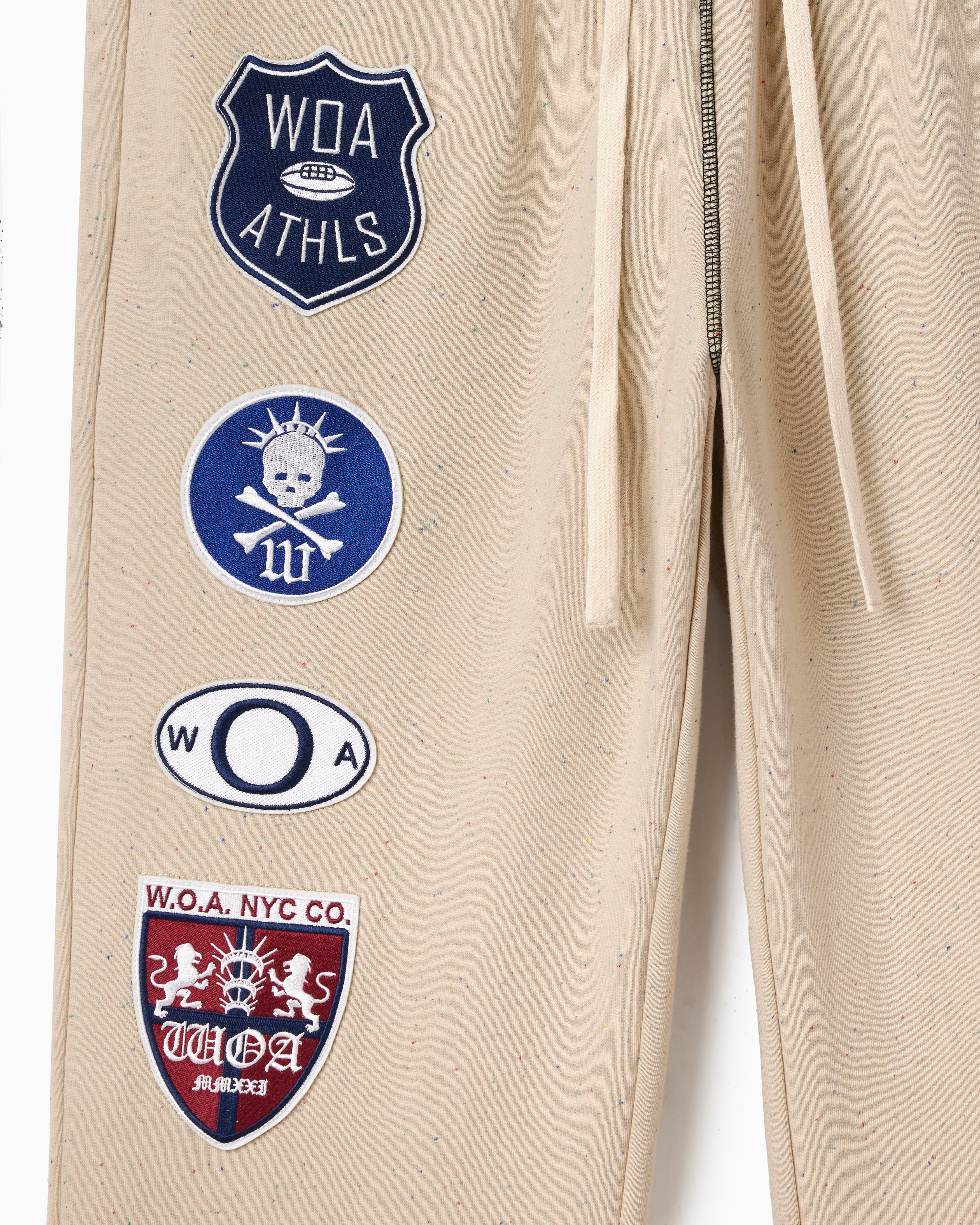 Wisdom Of Age Sandstone sweat pants with various patches including W.O.A and W.O.A.NYC.CO logos.