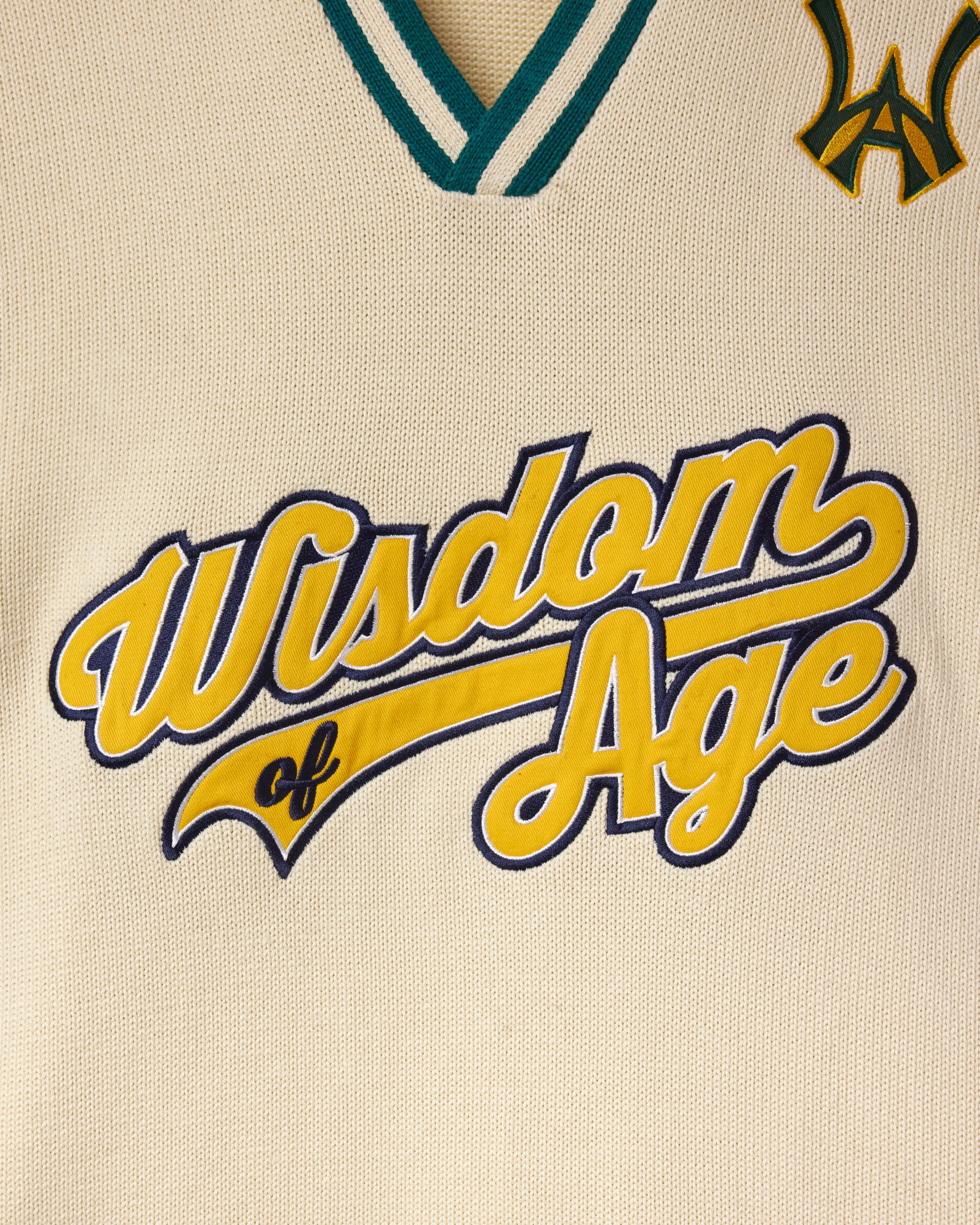 Cream knitted baseball jersey with 'Wisdom of Age' in script text in yellow and navy