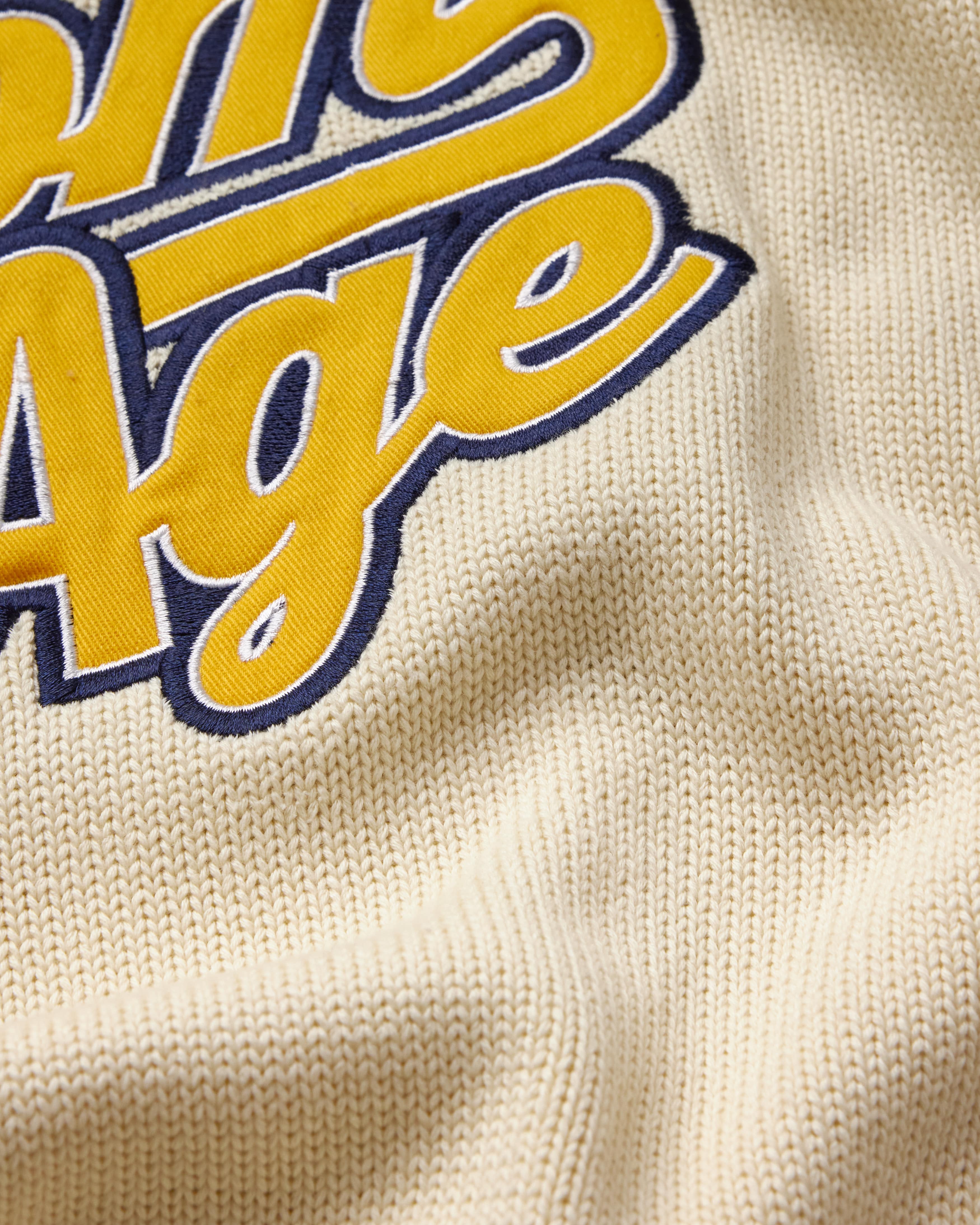 Close-up of a textured fabric with 'Wisdom Of Age' logo in yellow and blue.