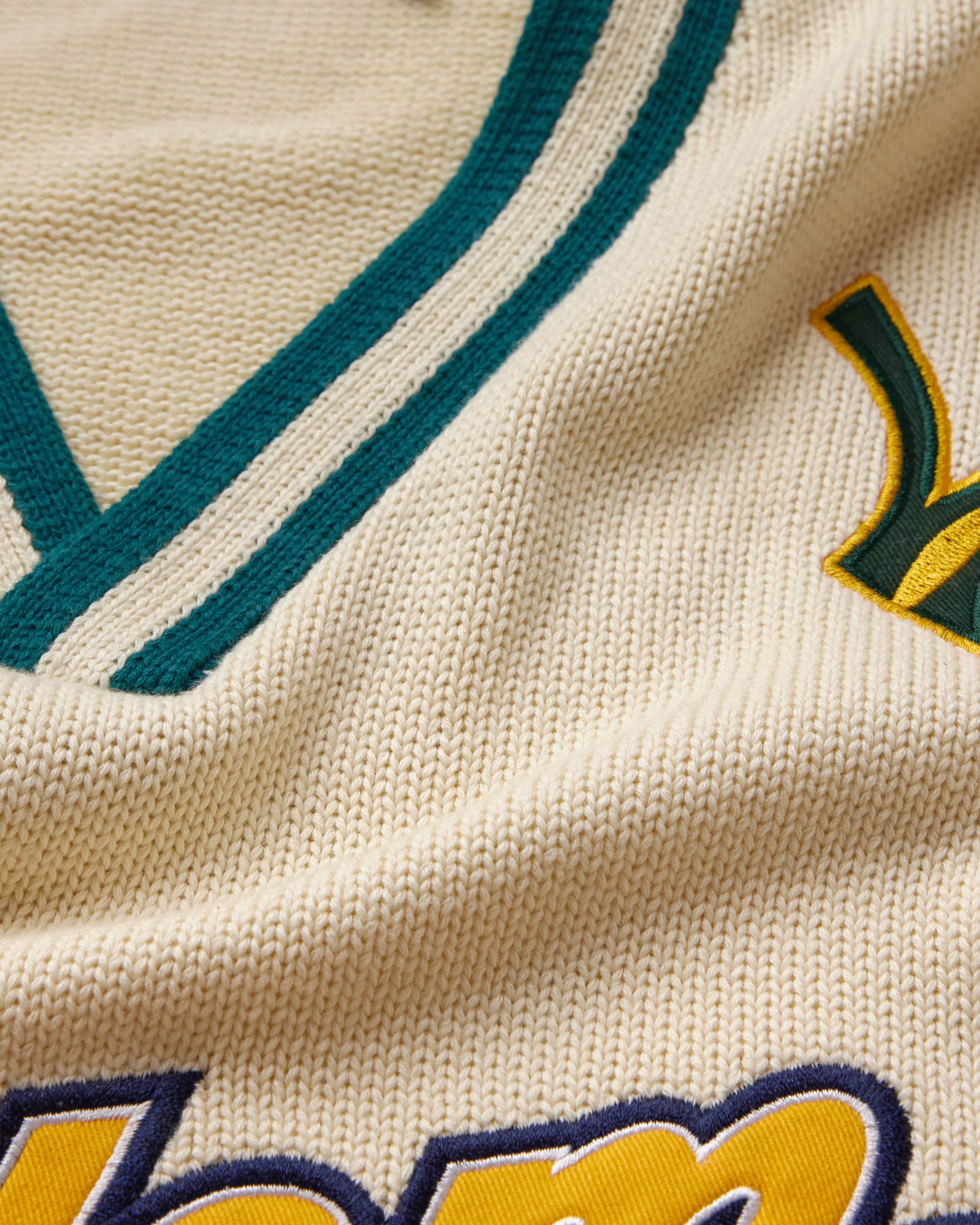 Close-up of a cream knitted jersey with green and yellow text and design elements.